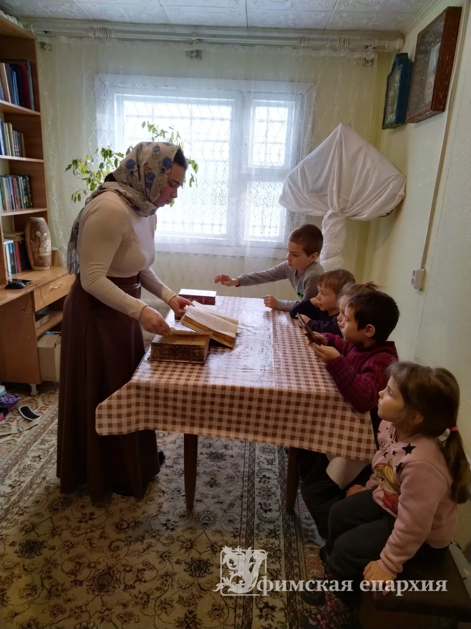 Преподаватель показывает детям старинные книги за столом в приходской комнате